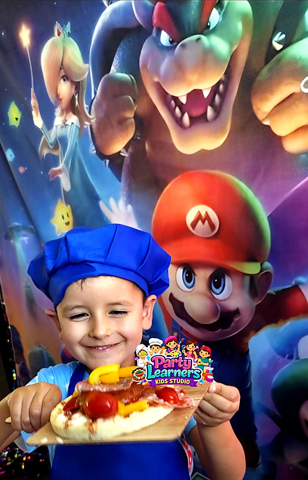 Boy in blue chef hat and Party Learners Kids Studio apron showing his decorated mini pizza at a Chef Party — Decorating Experience