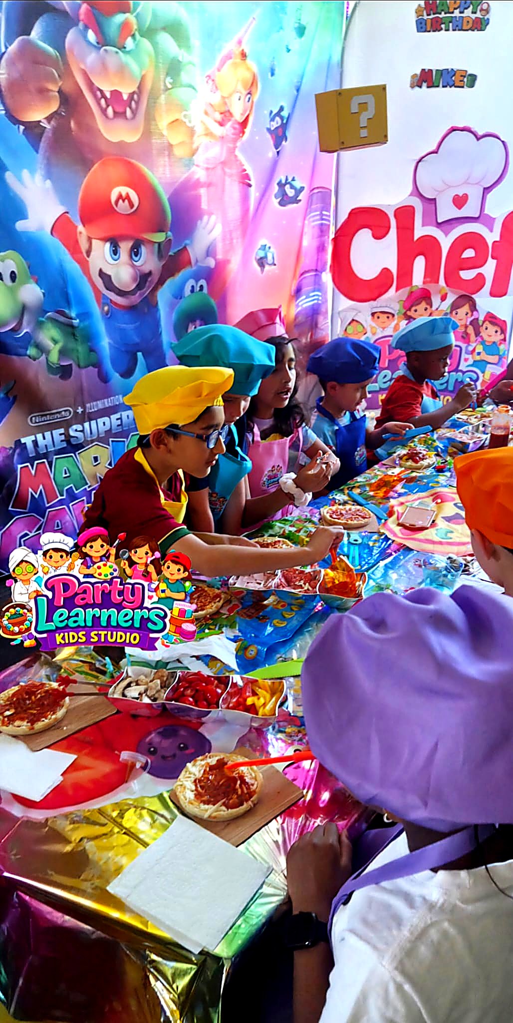 Kids in chef hats and aprons decorating their mini pizzas side-by-side at a Chef Party — Decorating Experience by Party Learners Kids Studio