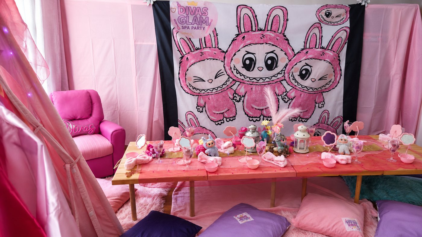 Divas Glam Spa Party setup with pink kawaii bunnies backdrop, pink chair, table with spa accessories and pillows at Party Learners Kids Studio