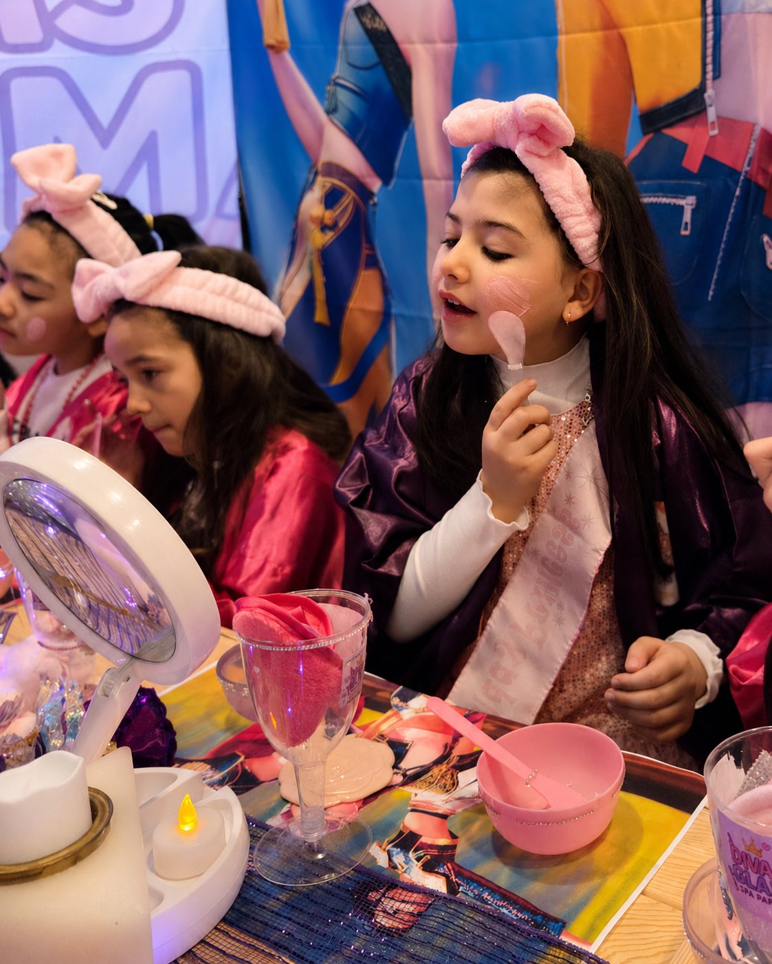 Girls in pink robes and bow headbands applying their own colorful spa-style masks at a Divas Glam Spa Party with K-Pop Demon Hunters tablemats and pink mirror