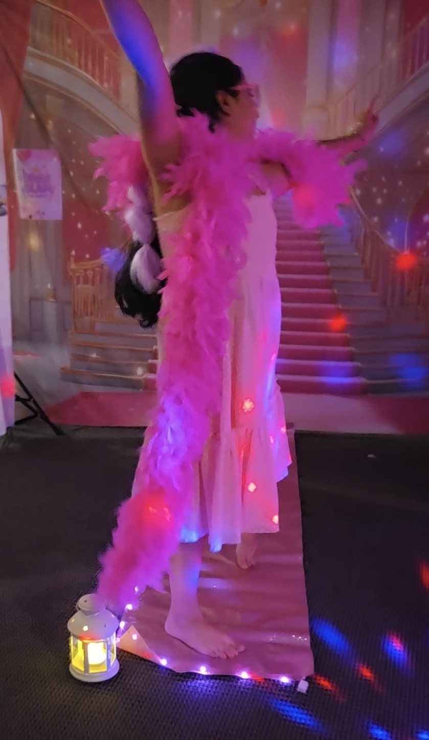 Birthday girl celebrating her runway moment with a hot pink feather boa on a glowing pink runway with light-up stars in front of the pink castle backdrop at a Divas Glam Spa Party
