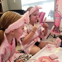 Two girls in pink robes and bow headbands enjoying mini makeovers with face masks at a Divas Glam Spa Party