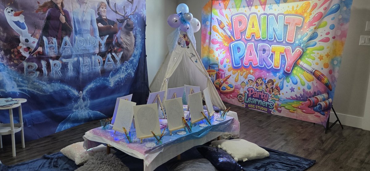 Frozen themed party setup with Happy Birthday backdrop, white teepee and paint easels